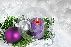 Christmas background with candle and decorations.Purple and silver Christmas balls over fir tree branches in the snow