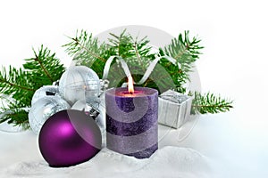 Christmas background with candle and decorations. Purple and silver Christmas balls over fir tree branches in the snow