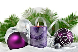 Christmas background with candle and decorations.Purple and silver Christmas balls over fir tree branches in the snow