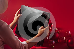 Christmas background, the child holds a tablet in his hands against the background of balls on a red