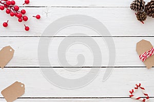Christmas background with christmas tags, holly berry, pine cons and candy cane on white wooden background.