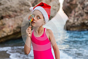 Christmas background: cute child in Santa hat celebrating New Year and Christmas on the beach, free space.