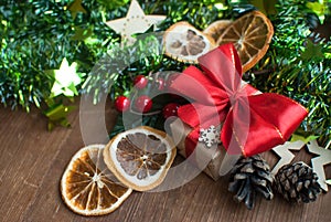 Christmas background with decorative composition of green tinsel, dried oranges, red berres, pine cone, gift with red bow and