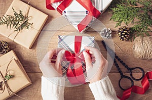 Christmas Background. Female Hands Tying A Red Bow. Woman Packing Christmas Gifts. Holiday Concept. Top View, Flat Lay, Advent