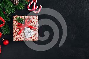 Christmas background with fir branches and a gift box with a red bow on a dark concrete background