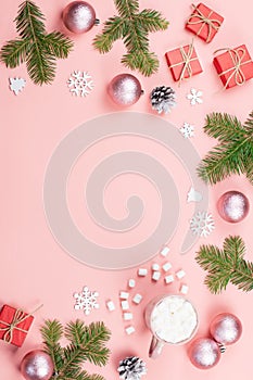 Christmas background with fir branches, lights, red giftboxes, pink decorations, hot drink with marshmallows on pink
