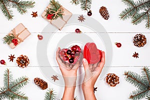 Christmas background with fir branches, pine cones, red decorations. Female hands holding Christmas gift. Xmas and Happy New Year