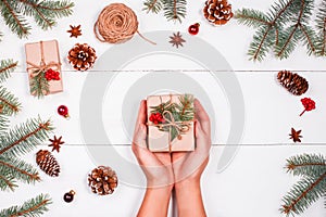 Christmas background with fir branches, pine cones, skein of jute, red decorations. Female hands holding Christmas gift. New Year