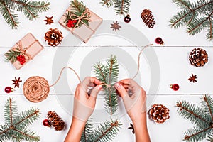 Christmas background with fir branches, pine cones, skein of jute, red decorations. Female hands. Xmas and Happy New Year composit