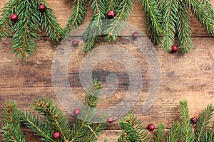 Christmas background with fir branches and red berries. Winter holidays frame with evegreen twigs on wooden board table.