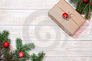 Christmas background - fir branches with red ornaments and a gift box on a white wood table. Flat layout, top view composition