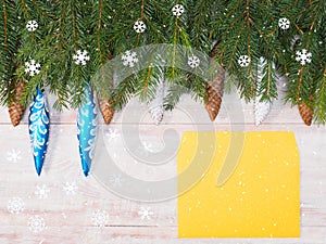 Christmas background with fir branches, snowflakes, toys, cones, yellow envelope on brown wooden background