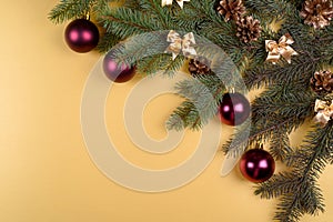 Christmas background with fir tree branches with glass balls, pine cones and bows on golden background, free space. Flat lay.