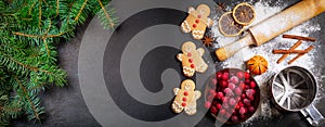 Christmas background. Fresh fir branches and gingerbread cookies with ingredients for christmas baking on dark background