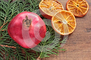 Christmas background with fruits and Christmas tree branches. Pomegranate, dried orange slices and green twigs on wooden table.