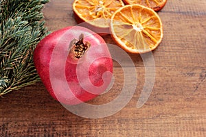 Christmas background with fruits and Christmas tree branches. Pomegranate, dried orange slices and green twigs on wooden table.