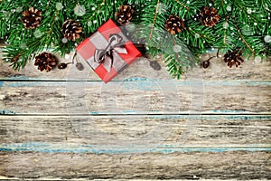 Christmas background with gift box, fir branch and conifer cone on wooden rustic board, festive snow effect, Christmas frame