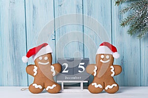 Christmas background with gingerbread men cookies in Santa hats and block calendar with 25 December, wooden background with fir
