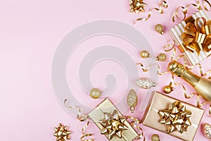 Christmas background with golden gift or present box, champagne and holiday decorations on pink pastel table top view. Flat lay.