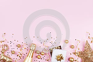 Christmas background with golden gift or present box, champagne and holiday decorations on pink pastel table top view. Flat lay.