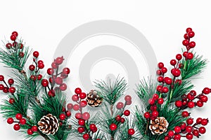 Christmas background with green fir tree branches, pine cones and red berries on a white backdrop. Template with copy space.