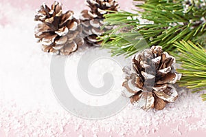 Christmas background, green pine branches, cones decorated with snow on snowy pink background. Creative composition with border