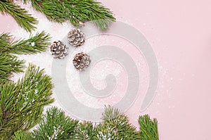 Christmas background, green pine branches, cones decorated with snow on snowy pink background. Creative composition with border