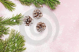 Christmas background, green pine branches, cones decorated with snow on snowy pink background. Creative composition with border