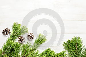 Christmas background, green pine branches, cones decorated with snow on white wooden table. Creative composition with border and c