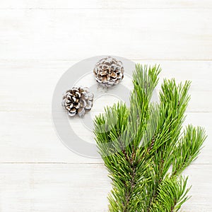Christmas background, green pine branches, cones decorated with snow on white wooden table. Creative composition with border and c