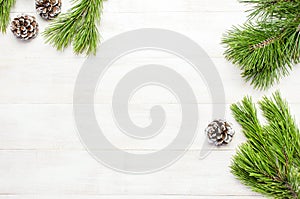 Christmas background, green pine branches, cones decorated with snow on white wooden table. Creative composition with border and c