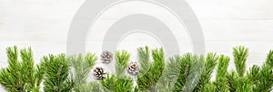 Christmas background, green pine branches, cones decorated with snow on white wooden table. Creative composition with border and c