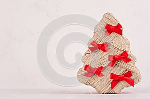 Christmas background - handmade New Year tree of jute with red ribbons on light white wooden board with copy space.