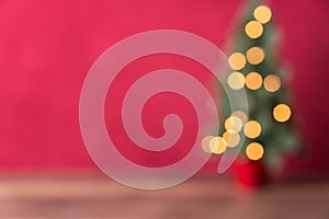 Christmas background, intentional blur of lit Christmas tree on wood table against red background