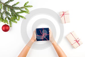 Christmas background with kid hands holding a present box, gift boxes and christmas tree branch and decoration.