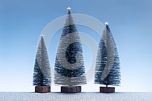 Minimalist scene with miniature fir trees and sparkly silver ground and blue sky