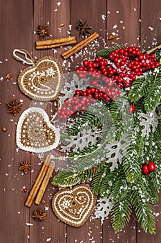 Christmas background. New Year fir tree, dog rose, fresh leaves, crocheted ginger cookies hearts, spices and artificial snow.