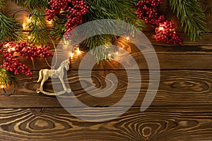 Christmas background. Nobilis fir branches, twigs with red berries, toy golden horse on brown wooden planks. Copy space, flat lay