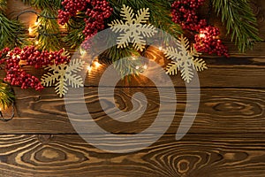 Christmas background. Nobilis fir branches, twigs with red berries, toy golden snowflakes on brown wooden planks. Copy space, flat
