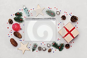 Christmas background of notebook, gift box, fir tree, conifer cone and holiday decorations on white table from above. Flat lay.