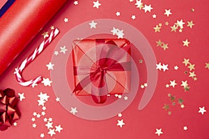 Christmas background, red gift box with ribbon bow on red background and golden sparkling conffeti, candy cane, bauble