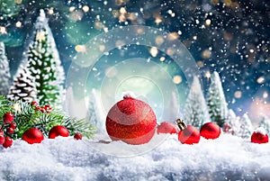 Christmas background with red ornaments in snow, bokeh and evergreen trees.
