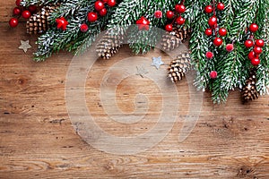 Christmas background. Snowy fir tree branches with fir cones and red berries on wooden board. Top view with space for text