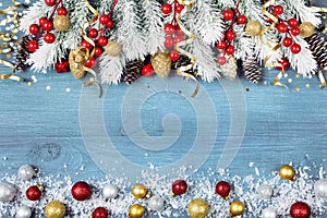 Christmas background with snowy fir tree and colorful holiday balls on blue wooden table top view. Greeting card with space