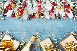 Christmas background with snowy fir tree, gift box, champagne and holiday decorations on blue wooden table top view. Greeting card