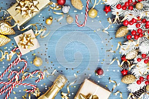 Christmas background with snowy fir tree, gift or present box, champagne and holiday decorations on blue wooden table top view.