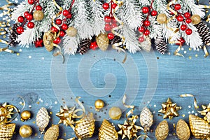 Christmas background with snowy fir tree and golden holiday decorations on blue wooden table top view. Greeting card.