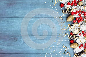 Christmas background with snowy fir tree and holiday decorations on blue wooden table top view. Greeting card with space for text.