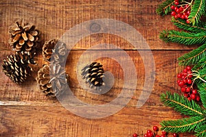 Christmas background. Spruce branches, red berries of potassium and pine cones on a wooden background