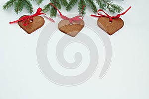 Christmas background . Three gingerbread hearts hanging under fir branch and against white background. Christmas spirit. W